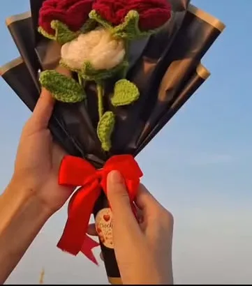Crochet bouquet of two red roses and one white rose in black wrap with a red bow, by Ilmaa