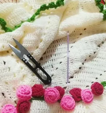 Pink and red crochet roses stitched onto a cream crochet piece, with yarn snips and a hook